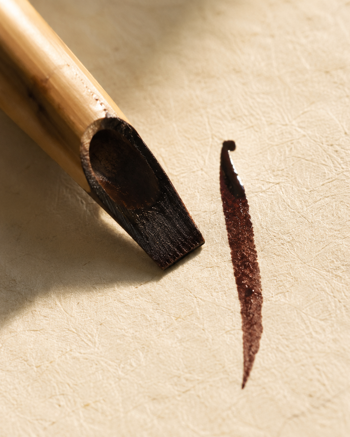 Un alif tracé à l’encre brune au calame de roseau sur un parchemin couleur crème